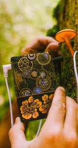 Pocket SCÍON Mycelium Edition held up to an orange mushroom on a mossy tree